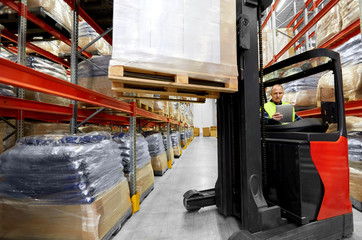 logistic business, shipment and loading concept - loader with tablet pc computer and cargo on forklift at warehouse