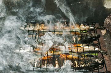 Mackerel fish grilled on iron plate in rural house fireplace closeup with white smoke