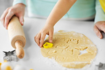 family, cooking and people concept - mother and little daughter with molds making cookies from dough at home kitchen