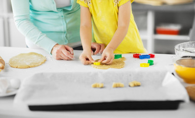 family, cooking and people concept - mother and little daughter with molds making cookies from dough at home kitchen