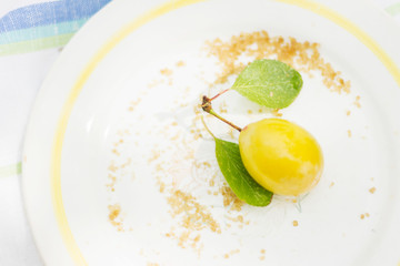 Yellow plum with green leaves and crystals of brown sugar on a decorated plate