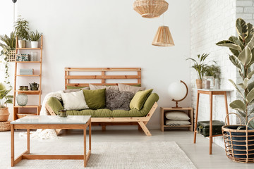 Pillows on green settee in natural botanic living room interior with wooden table and plants. Real...
