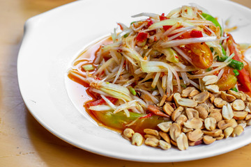 The close up of papaya salad with long bean tomato and peanut in the white dish on the wooden table. 