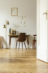 Wooden floor in classic home office interior with chair at desk next to gold lamp. Real photo