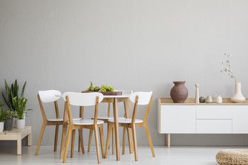 Wooden chairs at table in grey dining room interior with plants and white cupboard. Real photo