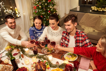 holidays and celebration concept - happy friends having christmas dinner at home, drinking red wine and clinking glasses