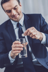 Treatment. Presentable pleasant man looking at the glass while putting down a pill in water