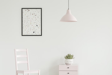 White chair next to cabinet with plant in simple living room interior with lamp and poster. Real photo