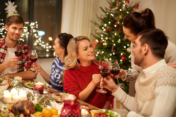 holidays and celebration concept - happy friends having christmas dinner at home, drinking red wine and clinking glasses