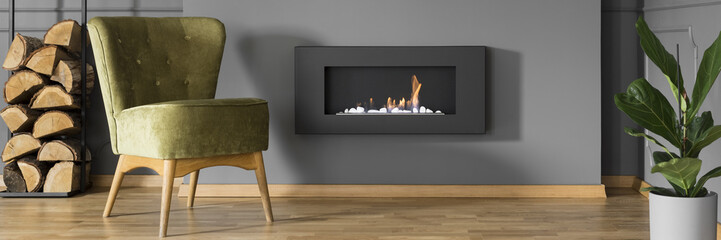 Chopped wood, an elegant, comfortable green armchair and a stylish bio fireplace in a dark,...