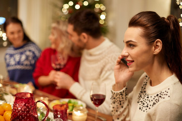 holidays, communication and celebration concept - close up of young woman calling on smartphone and having christmas dinner with friends at home