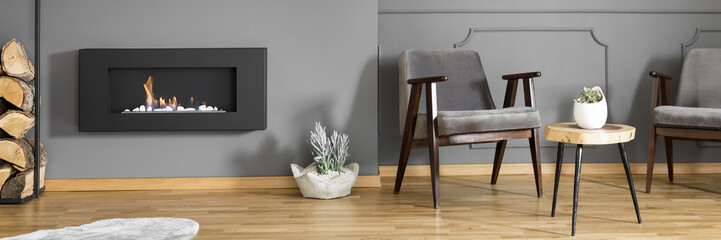 A side table between two elegant,comfortable armchairs and a pile of wood next to a modern...