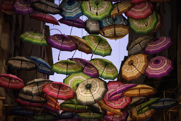Night shot of colorful umbrellas in small street in middle of city on blue evening sky background. Romantic walk in rainy day