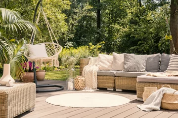 Foto op Canvas A big terrace with a comfortable leisure sofa with cushions, a table and a string swing in a green garden during sunny vacation. © Photographee.eu