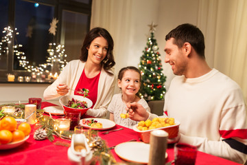 holidays, family and celebration concept - happy mother, father and little daughter having christmas dinner at home