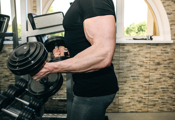 Man is training in the gym with weights. Young guy in trainers and sports clothes is doing exercises for good muscles. Fitness personal trainer is at work. Sport motivation healthy lifestyle.