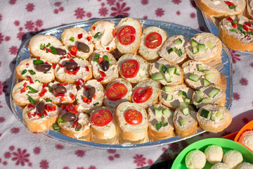 Variety of mini sandwiches with cheese cream, vegetables  roasted cherry tomatoes, olives, cucumber, spring onions, paprika, basil and other herbs. Fresh appetizer canape at the picnic outdoors