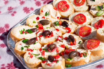 Variety of mini sandwiches with cheese cream, vegetables  roasted cherry tomatoes, olives, cucumber, spring onions, paprika, basil and other herbs. Fresh appetizer canape at the picnic outdoors