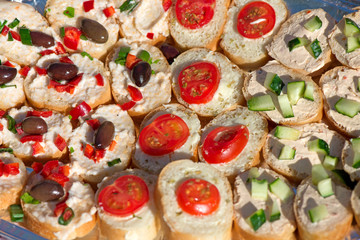 Variety of mini sandwiches with cheese cream, vegetables  roasted cherry tomatoes, olives, cucumber, spring onions, paprika, basil and other herbs. Fresh appetizer canape at the picnic outdoors