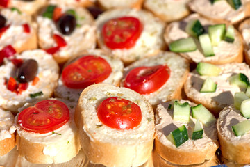 Variety of mini sandwiches with cheese cream, vegetables  roasted cherry tomatoes, olives, cucumber, spring onions, paprika, basil and other herbs. Fresh appetizer canape at the picnic outdoors