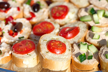 Variety of mini sandwiches with cheese cream, vegetables  roasted cherry tomatoes, olives, cucumber, spring onions, paprika, basil and other herbs. Fresh appetizer canape at the picnic outdoors
