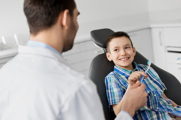 medicine, dentistry and healthcare concept - male dentist giving toothbrush to kid patient at...