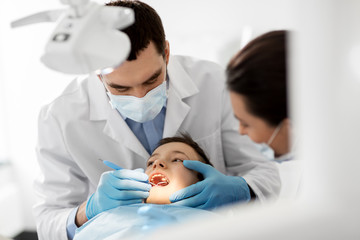 medicine, dentistry and healthcare concept - dentist with mouth mirror checking for kid patient...