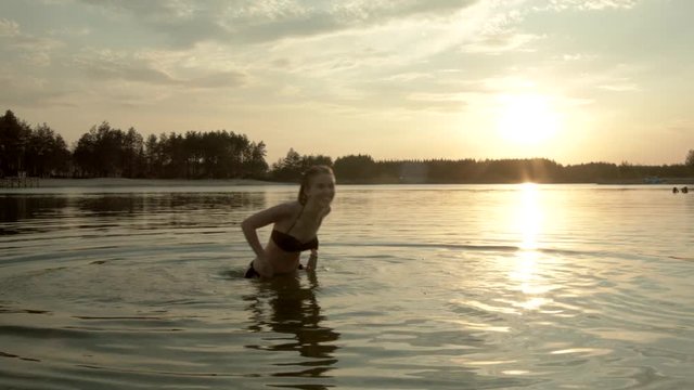 Beautiful girl, blond, funny dancing in the water of a forest lake and laughing.