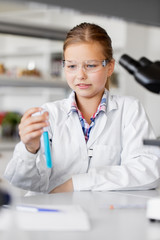 education, science and children concept - girl in goggles with test tube studying chemistry at school laboratory