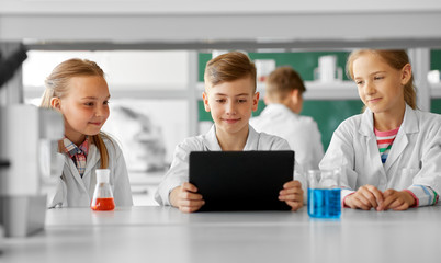 education, science and technology concept - kids with tablet pc computer studying chemistry at school laboratory