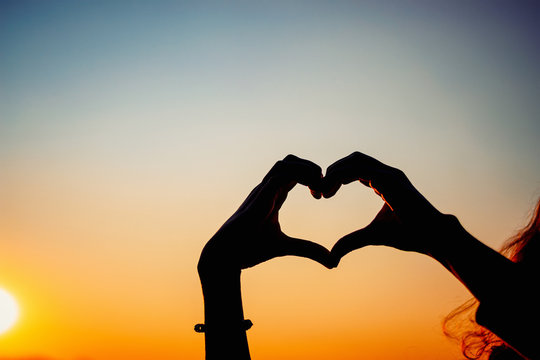 silhouette hands forming heart shape with sunset