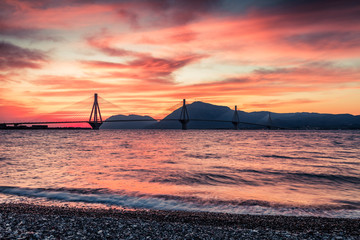 Dramatic red sky under a Rion-Antirion Bridge. Colorful spring scene on the Gulf of Corinth, Greece, Europe. Beauty of countryside concept background. Beauty of countryside concept background.