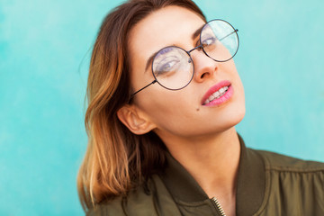 Fototapeta premium fashion girl in round glasses stands posing near a turquoise wall