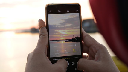 A woman is photographing a sunset with her cellphone