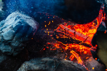 Smoldered logs burned in vivid fire close up. Atmospheric background with orange flame of campfire. Unimaginable detailed image of bonfire from inside with copy space. Smoke and glowing embers in air.