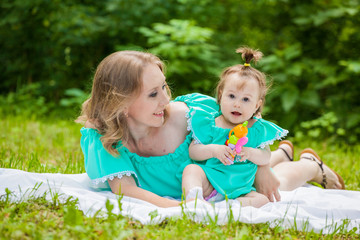Young mother and daughter in identical dresses lay on the grass