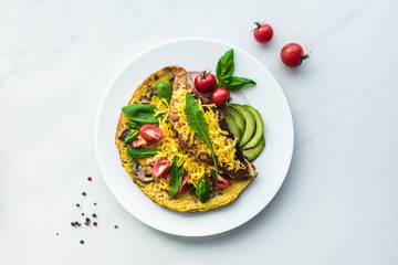 top view of homemade omelette with cherry tomatoes, avocado pieces and spinach on white marble surface