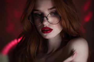 Redhead lady with freckless and long hair wearing eyeglasses looking aside over red lighting...