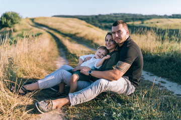 Naklejka na ściany i meble happy parents with adorable little son sitting together and smiling at camera rural trail