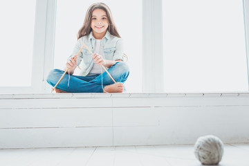 Knitting sticks. Little charming girl feeling joyful while playing with knitting sticks sitting...