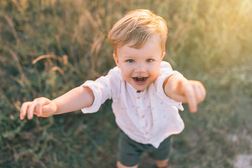 high angle view of adorable little boy reaching hands and smiling at camera outdoors