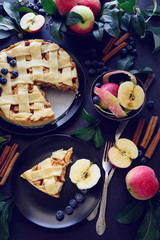 American tradition apple pie with apples, blueberry and cinnamon decorated apple leaves on dark wooden background. Top view. Flat lay. Still life. Toned
