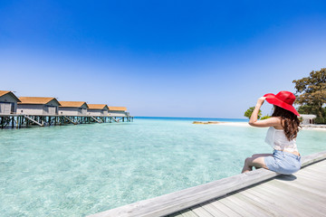 Fototapeta na wymiar Portrait of Asian young woman sitting on wooden bridge looking in villas over water with beautiful turquoise sea in Maldives tropical island,feeling relax and comfortable,Travel and Vacation Concept