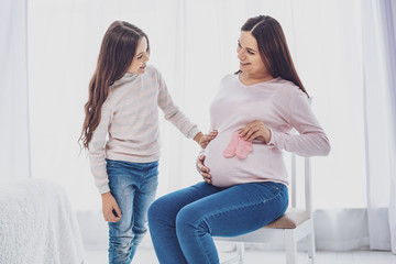 Just look. Pleased positive pregnant woman sitting on chair and looking at her delighted cute...