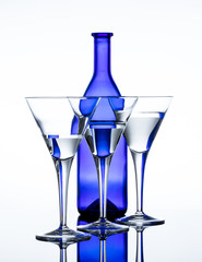 Three martinin glasses filled with a clear drink in front of a blue bottle