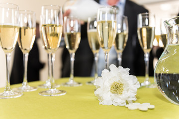 sparkling wine and champagne on a table with a white flower at a wedding, people in background