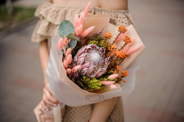 Woman in beige dress holding a nude colored bouquet of flowers with protea