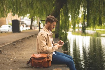 Man using digital tablet while sitting near lake side