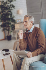 Try to remember. Senior male person sitting on his armchair while being deep in thoughts