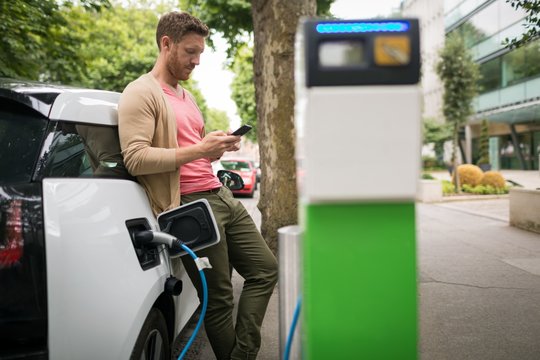 Man using mobile phone while charging electric car